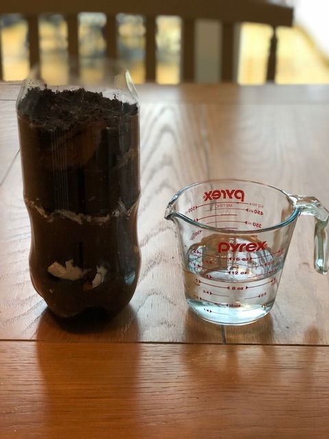 plastic bottle full of soil next to measuring glass with water in it